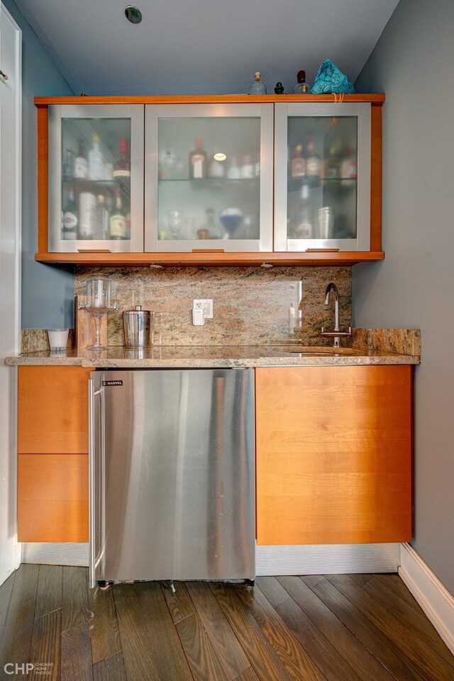 bar with backsplash, dark wood-type flooring, wet bar, freestanding refrigerator, and a sink