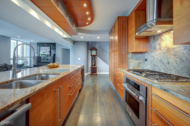 kitchen featuring a sink, brown cabinets, appliances with stainless steel finishes, and wall chimney range hood