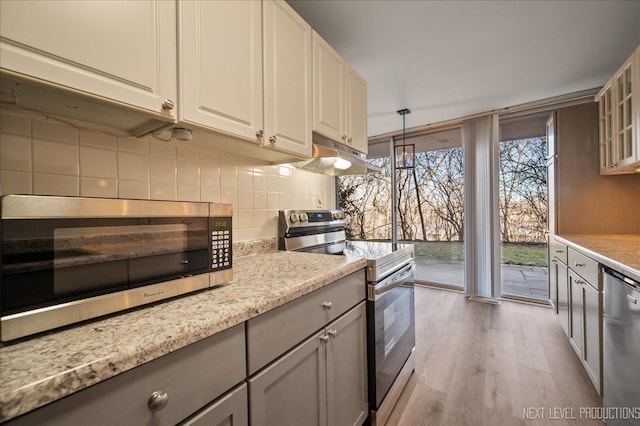 kitchen with stainless steel appliances, wood finished floors, gray cabinets, tasteful backsplash, and a wall of windows