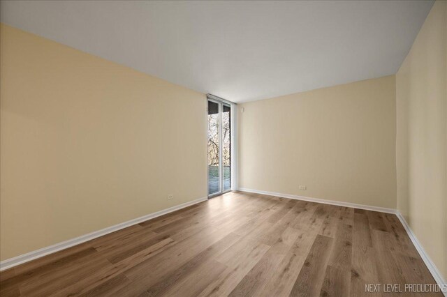 empty room with a wall of windows, light wood-type flooring, and baseboards