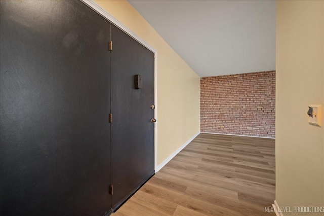 hall with light wood-type flooring, brick wall, and baseboards