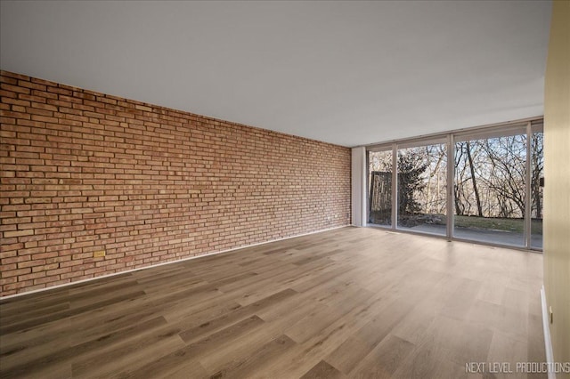 unfurnished room featuring brick wall and wood finished floors