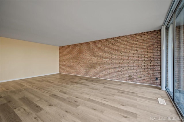 unfurnished room with brick wall, light wood-type flooring, visible vents, and baseboards