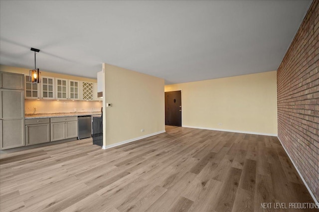 unfurnished living room with light wood-type flooring, baseboards, and brick wall