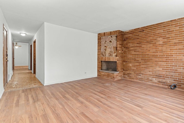 unfurnished living room with light wood-type flooring, baseboards, a stone fireplace, and brick wall