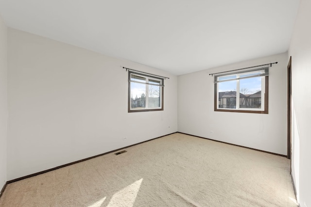 unfurnished room featuring carpet floors, visible vents, plenty of natural light, and baseboards