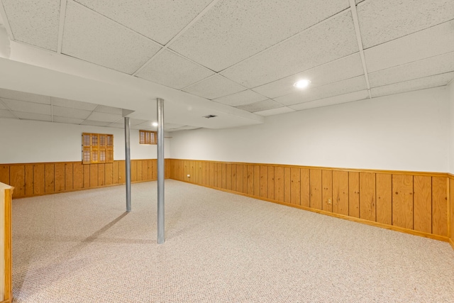 finished below grade area featuring carpet floors, a wainscoted wall, a drop ceiling, and wood walls