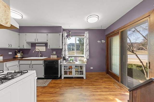 kitchen featuring baseboards, dishwasher, dark countertops, wood finished floors, and a sink