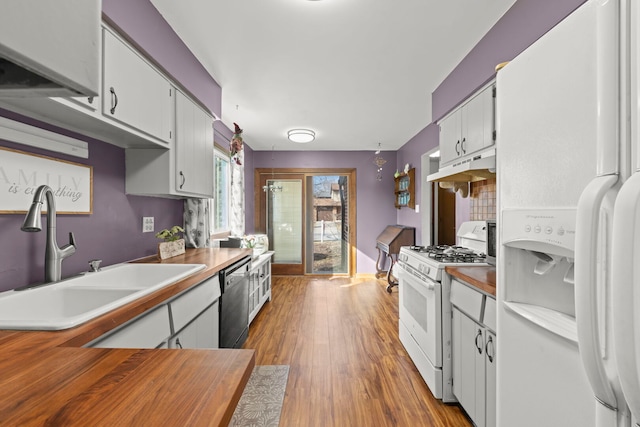 kitchen featuring under cabinet range hood, white appliances, wood finished floors, a sink, and white cabinetry