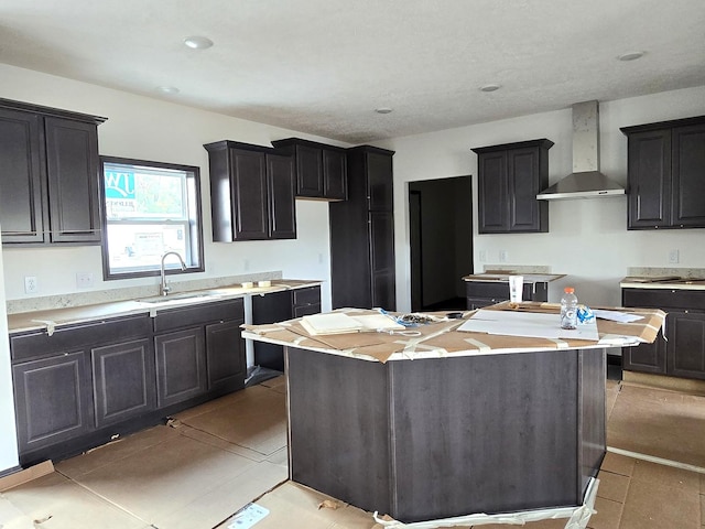 kitchen featuring light countertops, a kitchen island, wall chimney range hood, and a sink