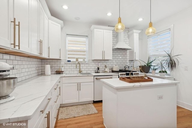 kitchen with wall chimney exhaust hood, white cabinetry, a sink, and a center island