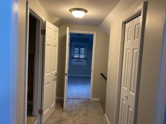 hallway with carpet floors, baseboards, and vaulted ceiling