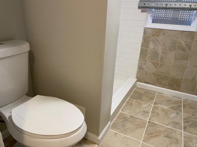 bathroom with baseboards, tiled shower, toilet, and tile patterned floors