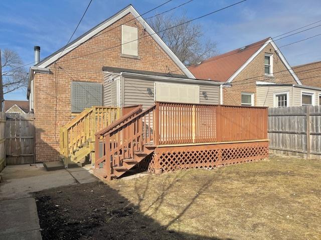 rear view of property with a deck, brick siding, and fence