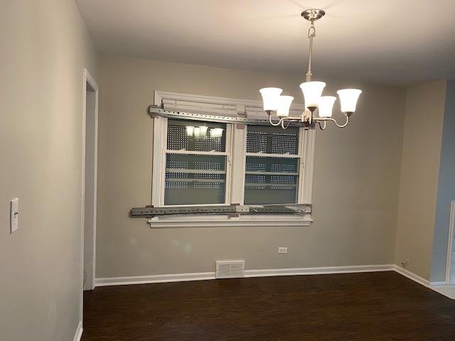 unfurnished room featuring an inviting chandelier, wood finished floors, visible vents, and baseboards