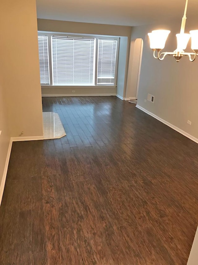 empty room with arched walkways, a chandelier, dark wood finished floors, and baseboards