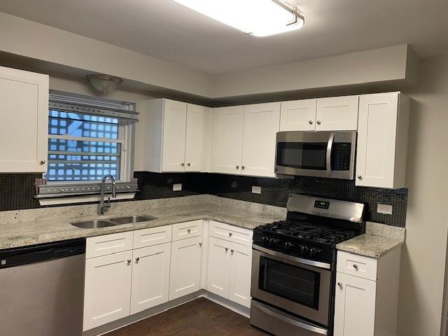 kitchen with tasteful backsplash, white cabinets, appliances with stainless steel finishes, light stone counters, and a sink