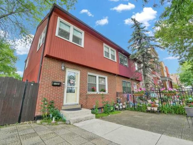 view of front facade with a patio area, fence, and brick siding