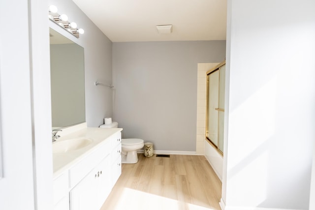 bathroom with visible vents, toilet, wood finished floors, combined bath / shower with glass door, and vanity