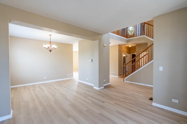 unfurnished room featuring visible vents, light wood-style flooring, stairway, baseboards, and a chandelier