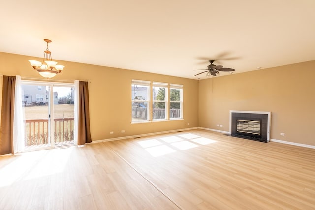 unfurnished living room with baseboards, ceiling fan with notable chandelier, a tiled fireplace, and light wood finished floors