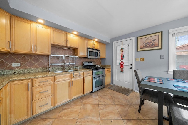 kitchen featuring light tile patterned floors, decorative backsplash, appliances with stainless steel finishes, light stone counters, and a sink