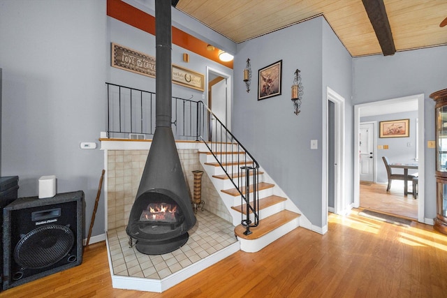 staircase with wood finished floors, wood ceiling, baseboards, beamed ceiling, and a wood stove