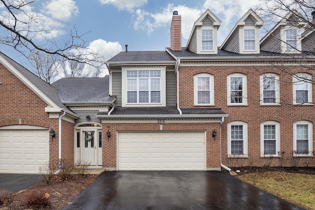 view of front of property with driveway, an attached garage, a chimney, and brick siding