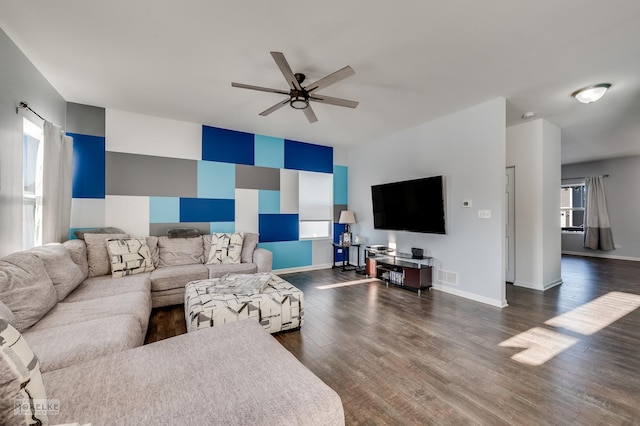 living area with dark wood finished floors, visible vents, an accent wall, a ceiling fan, and baseboards