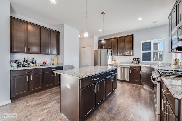 kitchen with dark wood finished floors, appliances with stainless steel finishes, a center island, dark brown cabinets, and pendant lighting