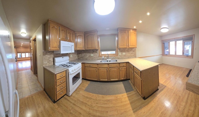 kitchen with a peninsula, white appliances, light wood-style flooring, and a sink