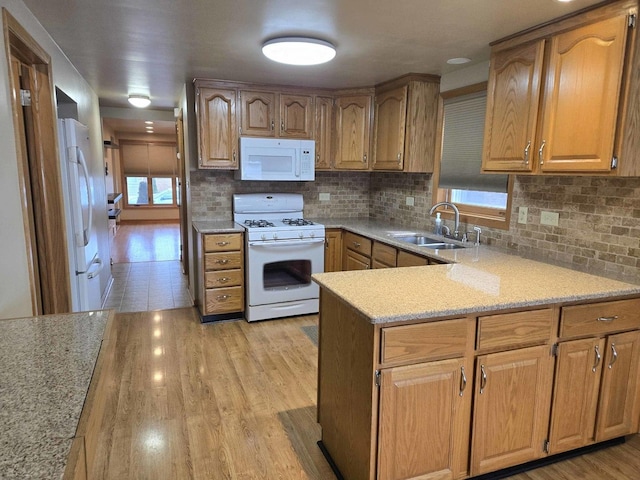 kitchen featuring a peninsula, white appliances, a sink, light wood-style floors, and tasteful backsplash