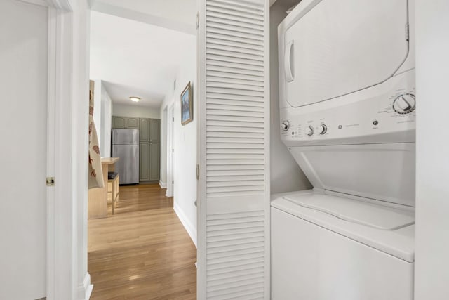 laundry area featuring laundry area, light wood-style flooring, stacked washer and clothes dryer, and baseboards