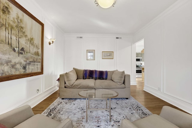 living area featuring ornamental molding, a decorative wall, and wood finished floors