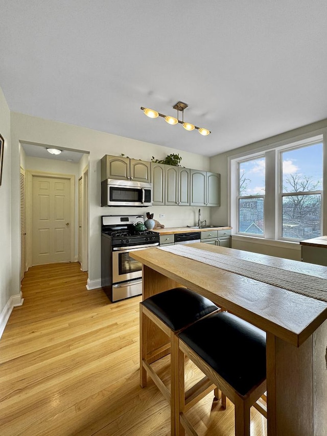 kitchen with appliances with stainless steel finishes, gray cabinets, baseboards, and light wood finished floors