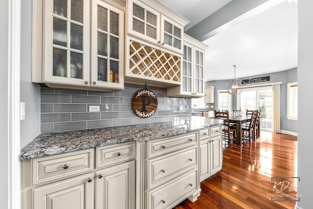 kitchen with decorative light fixtures, dark wood finished floors, decorative backsplash, glass insert cabinets, and stone countertops