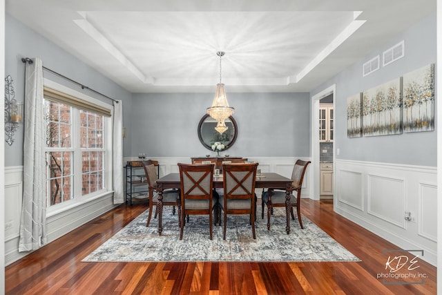 dining space featuring dark wood-type flooring, a raised ceiling, visible vents, and a wainscoted wall