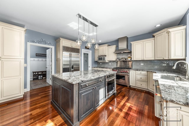 kitchen featuring a sink, high quality appliances, a center island, light stone countertops, and wall chimney exhaust hood