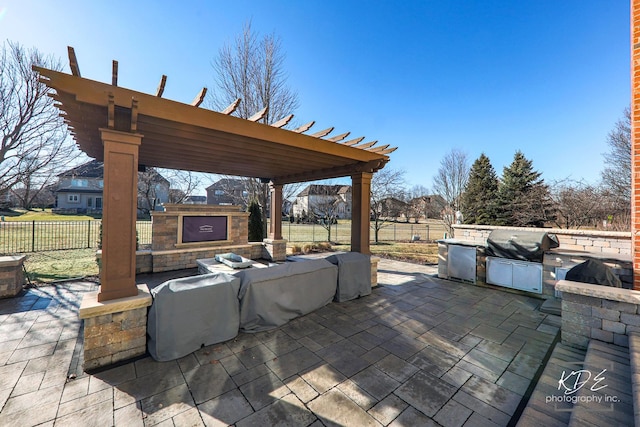 view of patio / terrace featuring fence, exterior fireplace, an outdoor kitchen, and a pergola