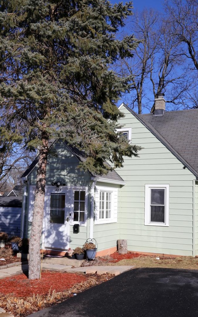 view of side of home featuring entry steps, a shingled roof, and a chimney