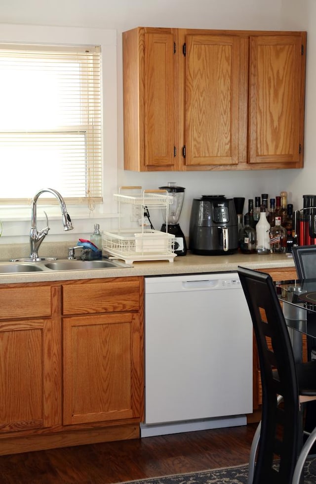 kitchen with dark wood-style flooring, light countertops, brown cabinetry, a sink, and dishwasher