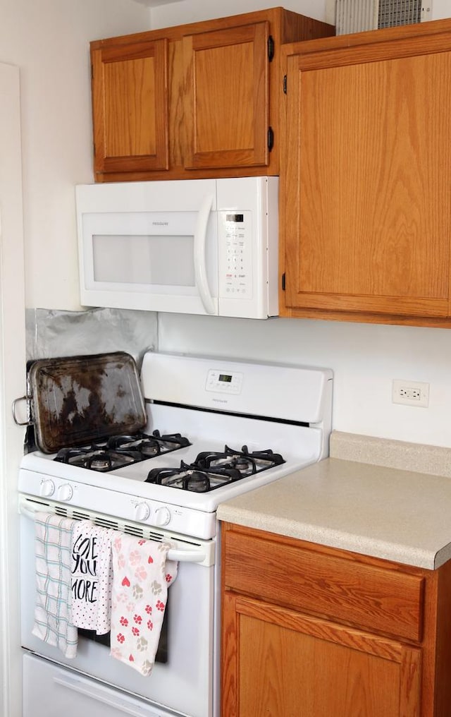 kitchen with brown cabinetry, white appliances, and light countertops