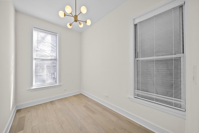 unfurnished room with baseboards, light wood-type flooring, and a notable chandelier