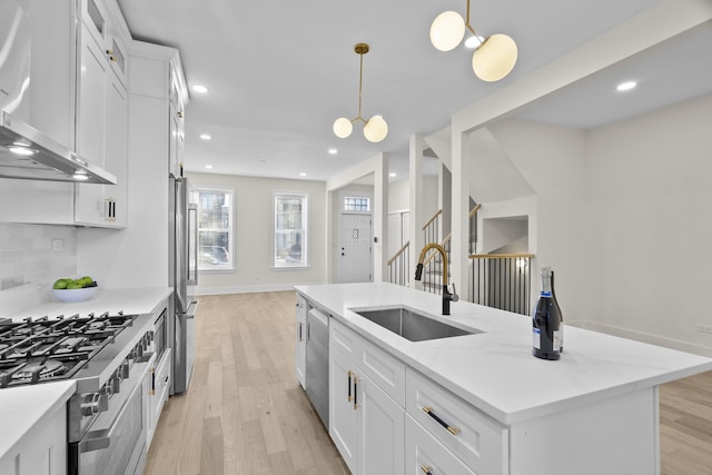 kitchen with white cabinets, wall chimney exhaust hood, hanging light fixtures, a kitchen island with sink, and a sink