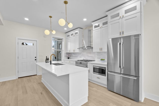 kitchen with a sink, light countertops, appliances with stainless steel finishes, wall chimney exhaust hood, and glass insert cabinets