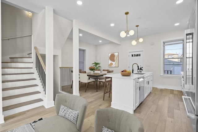 kitchen featuring white cabinets, a kitchen island with sink, light countertops, pendant lighting, and a sink