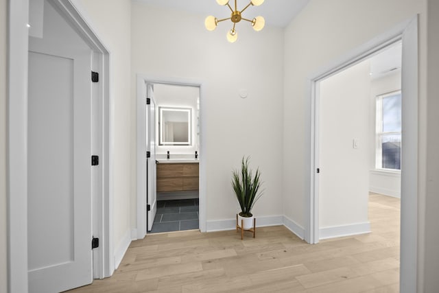 hallway featuring light wood-type flooring, an inviting chandelier, and baseboards