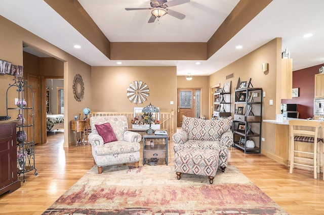 living room with baseboards, ceiling fan, a tray ceiling, light wood-style floors, and recessed lighting