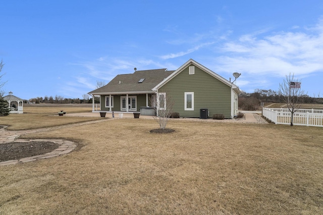 back of property with central AC, fence, and a lawn