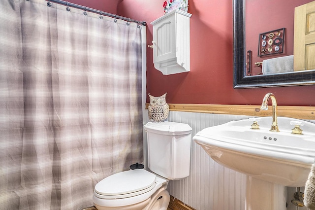 bathroom featuring a wainscoted wall, a sink, toilet, and a shower with curtain